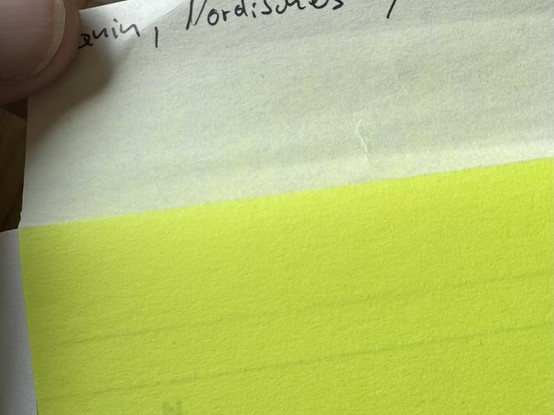 Grellgelbes Postit am oberen Rand einer Buchseite, der Teil der rausguckt, verblichen.